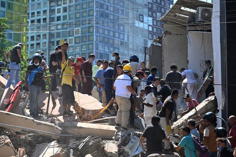 Equipos de rescate y ciudadanos trabajan en los escombros de un edificio colapsado en Cali, con torre de vidrio al fondo